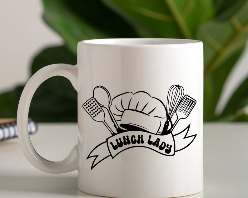 May include: White ceramic mug with a black and white illustration of a chef's hat, kitchen utensils, and the text "Lunch Lady".