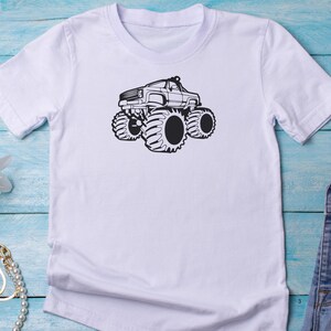 May include: White t-shirt with a black graphic of a monster truck with large tires.