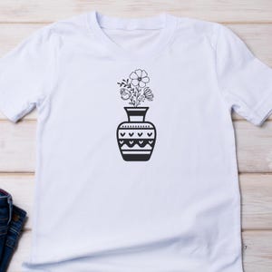 May include: White t-shirt with a black and white graphic of a vase with flowers. The vase has a geometric pattern.