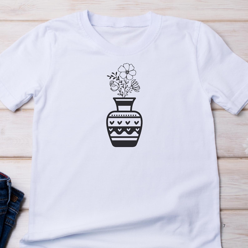 May include: White t-shirt with a black and white graphic of a vase with flowers. The vase has a geometric pattern.