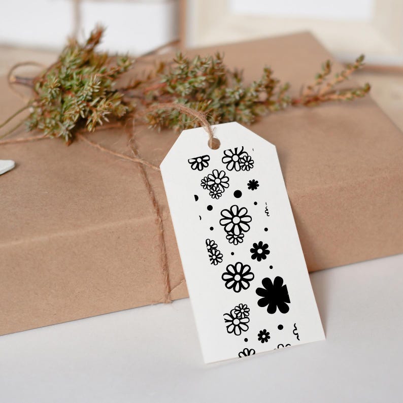 May include: A white gift tag with a black and white floral design. The tag is tied with twine to a brown paper wrapped gift box.