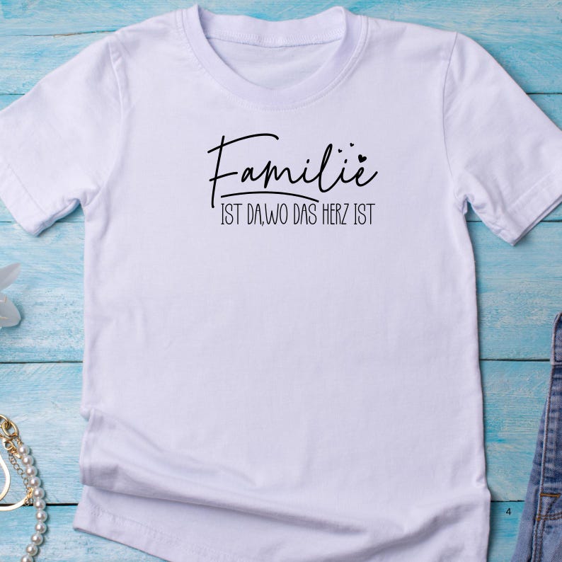 May include: White t-shirt with black text that reads "Familie ist da, wo das Herz ist" which translates to "Family is where the heart is".