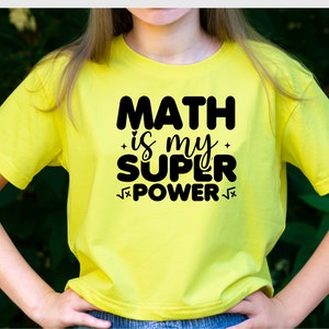 Puede incluir: Una camiseta amarilla con texto negro que dice "MATH is my SUPER POWER" con un s&iacute;mbolo de ra&iacute;z cuadrada antes y despu&eacute;s de la palabra "POWER".