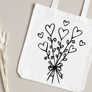 May include: A white tote bag with a black design of a bouquet of hearts with leaves and a bow.