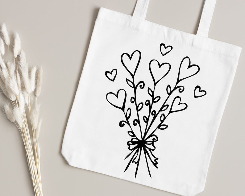 May include: A white tote bag with a black design of a bouquet of hearts with leaves and a bow.