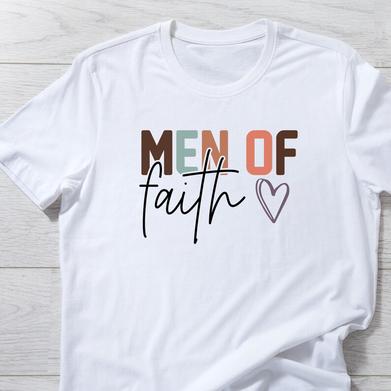 May include: White t-shirt with the text "MEN OF faith" in colorful letters and a small heart.