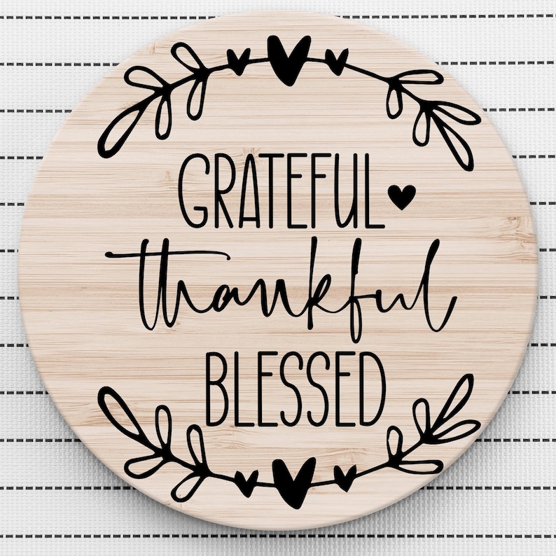 May include: Round wooden sign with the words "Grateful Thankful Blessed" in black script lettering. The sign is decorated with a wreath of leaves and hearts.
