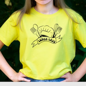 May include: A yellow t-shirt with a black graphic of a chef's hat, kitchen utensils, and the text "Lunch Lady".