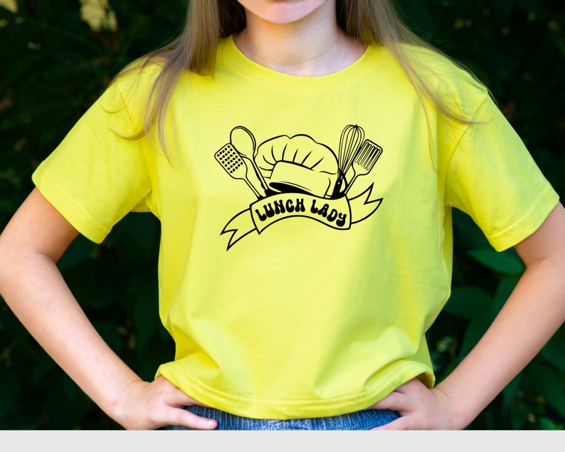 May include: A yellow t-shirt with a black graphic of a chef's hat, kitchen utensils, and the text "Lunch Lady".