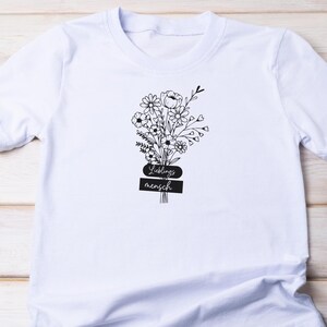 May include: White t-shirt featuring a black floral bouquet design with the words "Lieblingsmensch" in a stylized font. The bouquet includes various flowers and foliage, creating a delicate and artistic look. A casual and comfortable tee.
