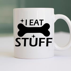 Puede incluir: Taza de caf&eacute; de cer&aacute;mica blanca con un gr&aacute;fico de hueso negro y el texto "I EAT STUFF" impreso en ella.