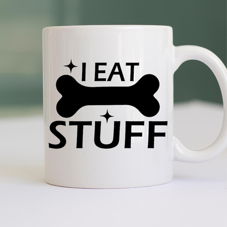 Puede incluir: Taza de caf&eacute; de cer&aacute;mica blanca con un gr&aacute;fico de hueso negro y el texto "I EAT STUFF" impreso en ella.