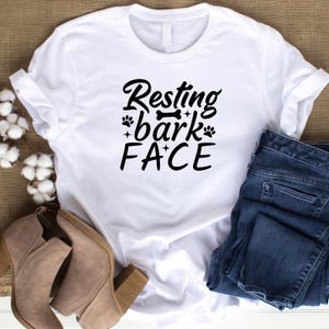 Puede incluir: Camiseta blanca con texto negro que dice "Resting bark face" con huellas de patas y un gr&aacute;fico de hueso.