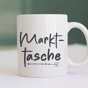 Pu&ograve; includere: Tazza in ceramica bianca con la scritta "Markt-Tasche" in corsivo nero, accompagnata da una freccia decorativa. La tazza ha un manico curvo ed &egrave; adatta per bevande calde o fredde.