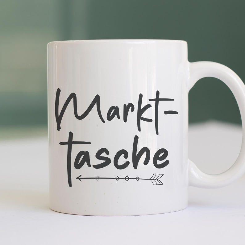 Pu&ograve; includere: Tazza in ceramica bianca con la scritta "Markt-Tasche" in corsivo nero, accompagnata da una freccia decorativa. La tazza ha un manico curvo ed &egrave; adatta per bevande calde o fredde.