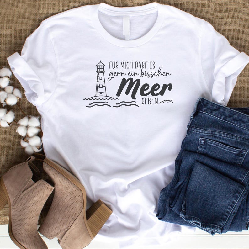 Puede incluir: Camiseta blanca con un gr&aacute;fico de faro y el texto "F&uuml;r mich darf es gern ein bisschen Meer geben."