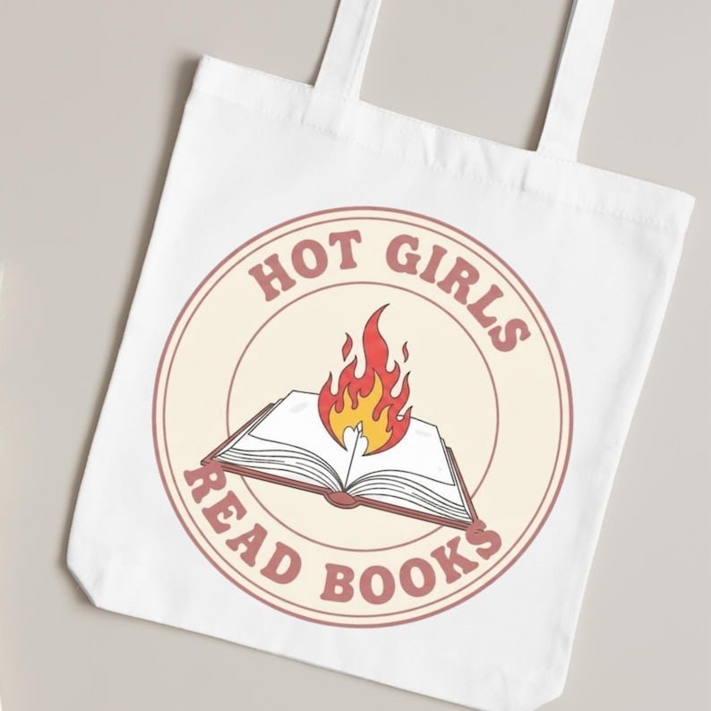 K&ouml;nnte beinhalten: Wei&szlig;er Stoffbeutel mit einem kreisf&ouml;rmigen Aufdruck. Der Aufdruck zeigt den Text "HOT GIRLS READ BOOKS" und ein offenes Buch mit roten, orangefarbenen und gelben Flammen. Der Beutel hat zwei wei&szlig;e Griffe.