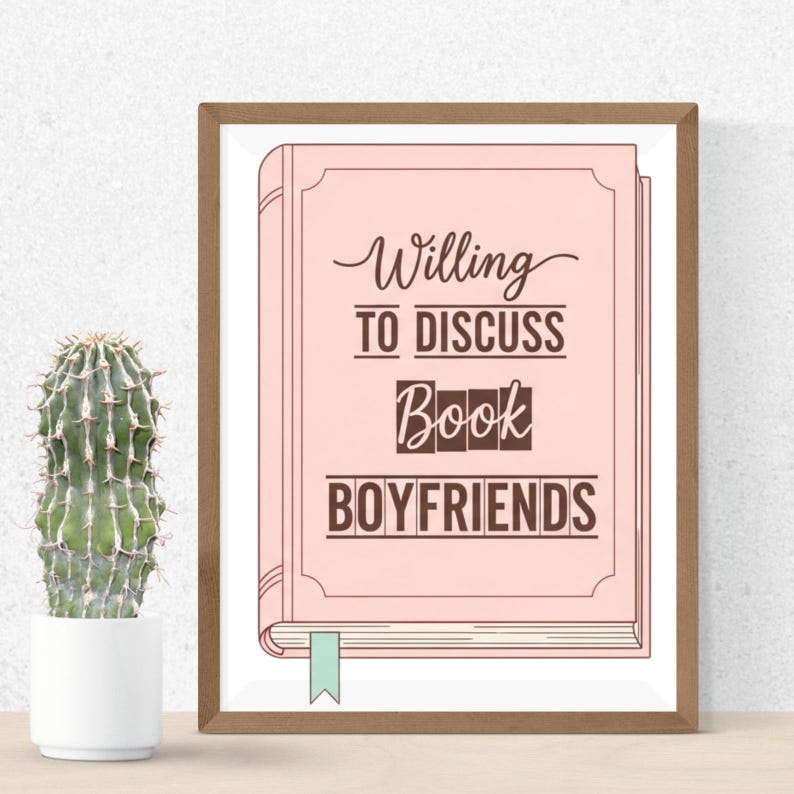 K&ouml;nnte beinhalten: Gerahmter Druck mit einem rosa Buchdesign und dem Text "Willing to Discuss Book Boyfriends". Der Text ist in Schreibschrift und Blockbuchstaben gehalten. Ein gr&uuml;nes Lesezeichen ist sichtbar. Links ist ein Kaktus in einem wei&szlig;en Topf.