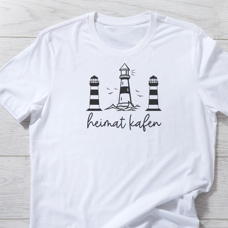 Puede incluir: Camiseta blanca con un gr&aacute;fico en blanco y negro de tres faros y el texto "heimat kafen".