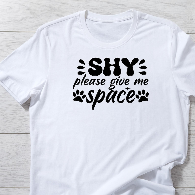 Puede incluir: Camiseta blanca con texto negro que dice "SHY please give me space" con huellas de patas a cada lado de la palabra "space".