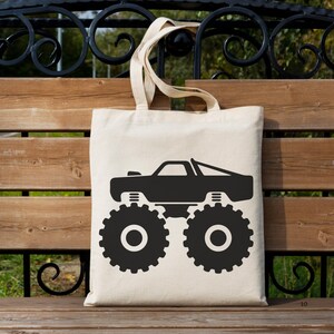 May include: A white canvas tote bag with a black silhouette of a monster truck. The truck has large tires and a raised chassis.
