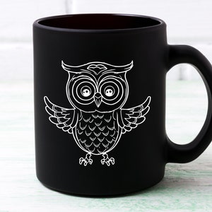 May include: Black ceramic coffee mug with a white outline of an owl with large eyes. The owl is facing forward with its wings spread out.
