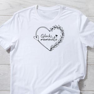May include: White t-shirt with a black heart design and the text "Gl&uuml;cks momento" inside the heart.