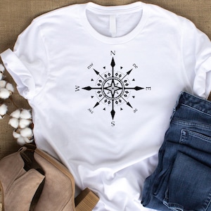 May include: White t-shirt with a black compass design featuring the cardinal directions and points of the compass. The compass is centered on the shirt and has a star in the middle.