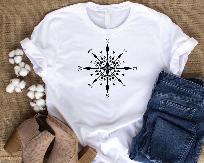 May include: White t-shirt with a black compass design featuring the cardinal directions and points of the compass. The compass is centered on the shirt and has a star in the middle.