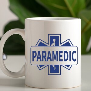 May include: White ceramic coffee mug with a blue star of life symbol and the word "PARAMEDIC" printed on it.