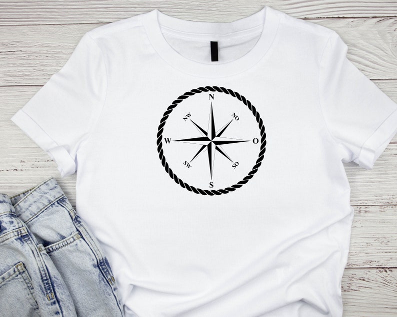May include: White t-shirt with a black compass design. The compass has a rope border and points to the cardinal directions: North, South, East, and West.
