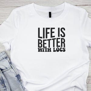 May include: White t-shirt with black text that reads "Life is better with locs".