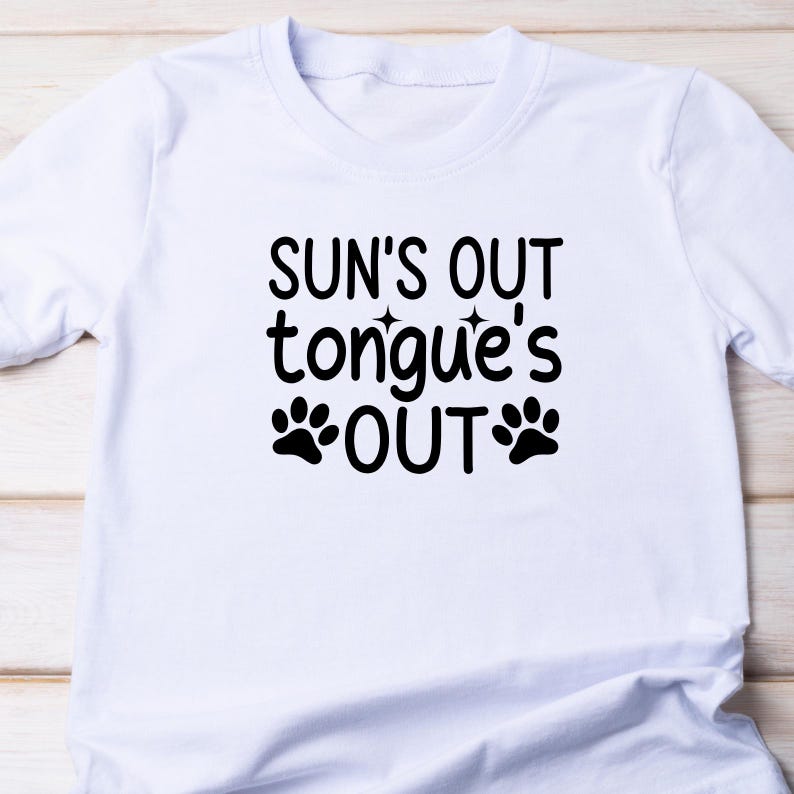 Puede incluir: Camiseta blanca con texto negro que dice "Sun's out tongue's out" con dos huellas de pata a cada lado de la palabra "out".