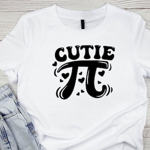 Puede incluir: Camiseta blanca con texto negro que dice "cutie pi" con un s&iacute;mbolo pi estilizado y corazones alrededor.