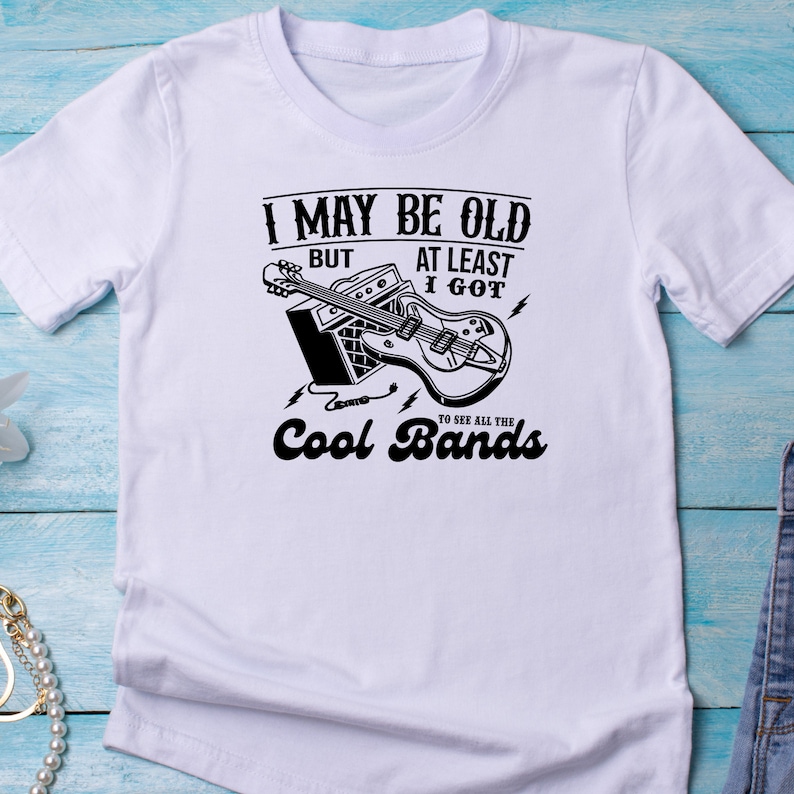May include: White t-shirt with a black graphic of a guitar and amplifier. The text on the shirt reads "I may be old but at least I got to see all the cool bands."