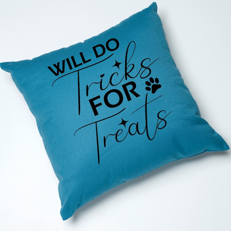 Puede incluir: Una almohada de color azul turquesa con el texto "Will Do Tricks For Treats" en letras negras. Tambi&eacute;n se incluye una huella de pata y dos estrellas en el dise&ntilde;o.