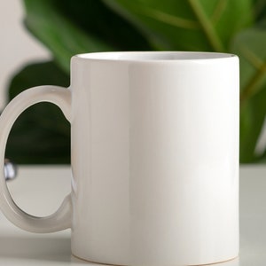 May include: A white ceramic mug with a rounded handle. The mug is empty and ready to be filled with a hot beverage.