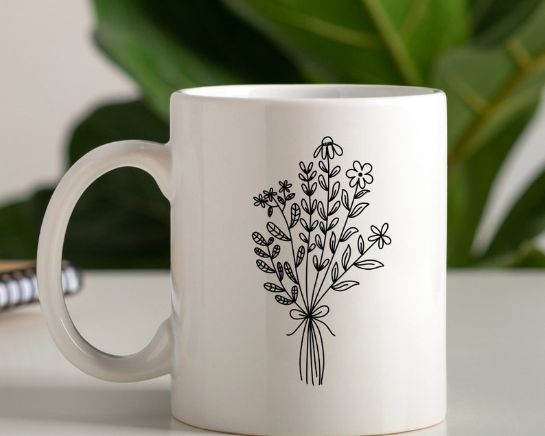 May include: White ceramic mug with a black line drawing of a bouquet of flowers. The flowers are stylized and have simple lines.