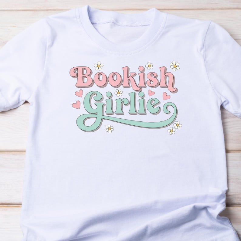K&ouml;nnte beinhalten: Wei&szlig;es T-Shirt mit dem Aufdruck "Bookish Girlie" in Rosa und Mintgr&uuml;n, verziert mit Blumen und Herzen. Das Design ist auf einem leichten, weichen Stoff gedruckt, ideal f&uuml;r den t&auml;glichen Gebrauch.