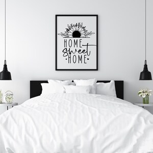 May include: Black and white print with a sunflower design and the text "Home Sweet Home" in a white bedroom with a white bed and black bedside tables.