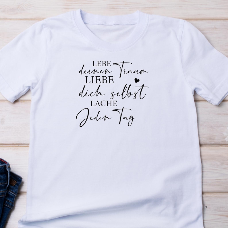 May include: White t-shirt with black text that reads "Lebe deinen Traum LIEBE dich selbst LACHE Jeden Tag".