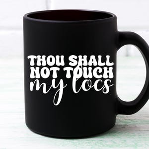 May include: Black ceramic coffee mug with white text that reads "Thou Shall Not Touch My Locs".