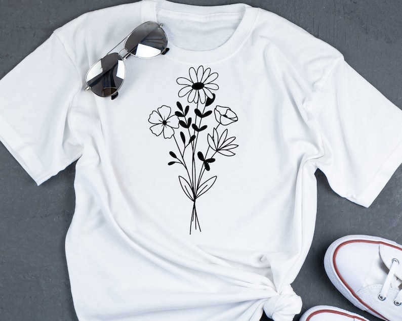 May include: White t-shirt with a black floral design featuring a daisy, a poppy, and other flowers.