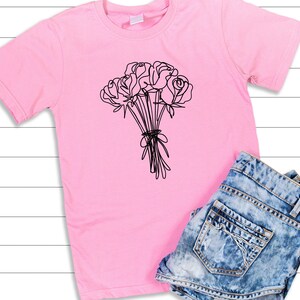 May include: A pink t-shirt with a black line drawing of a bouquet of roses.