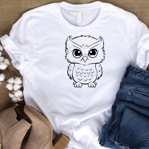 May include: White t-shirt with a black and white cartoon owl graphic.