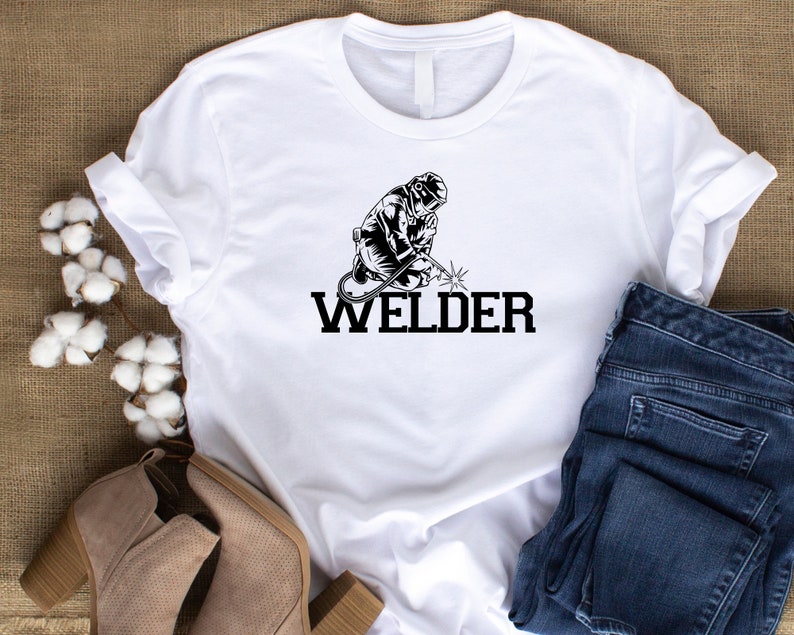 Puede incluir: Camiseta blanca con una ilustraci&oacute;n en blanco y negro de un soldador y la palabra "WELDER" en texto negro.