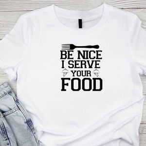 May include: White t-shirt with black text that reads "Be Nice I Serve Your Food" with a fork and plate graphic.