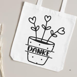 May include: White tote bag with a black and white illustration of a potted plant with three hearts for flowers. The pot has the word "DANKE" written on it.