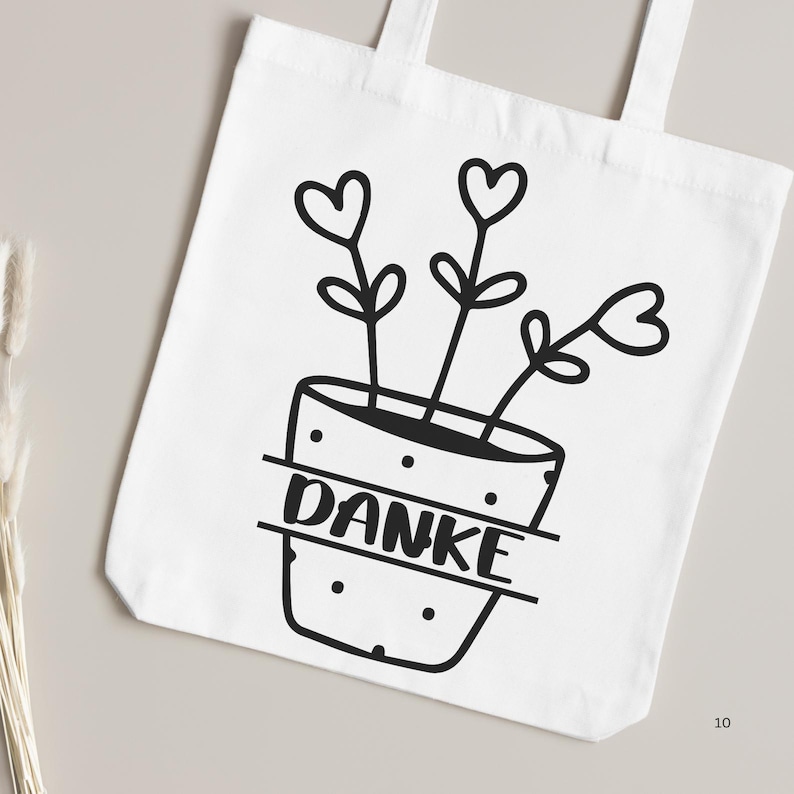 May include: White tote bag with a black and white illustration of a potted plant with three hearts for flowers. The pot has the word "DANKE" written on it.