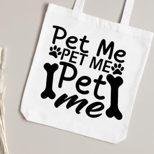 Puede incluir: Bolsa de tela blanca con texto negro que dice "Pet Me Pet Me Pet Me" con huellas de patas y gr&aacute;ficos de huesos.